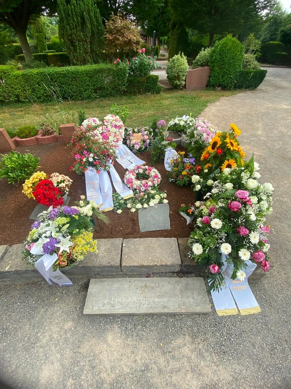 Grab mit Blumenkränzen, Schleifen und bunten Trauersträußen